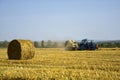 Harvested wheat field with large round bales of straw in summer. Tractor forming bales is visible background. Farmland Royalty Free Stock Photo