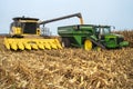 Harvester combine dumping corn into grain cart on back of tractor