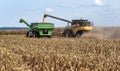 Harvester combine dumping corn into grain cart on back of tractor