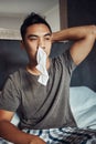 Has anybody seen my tissue. Shot of a young man blowing his nose while recovering from an illness in bed at home. Royalty Free Stock Photo