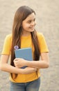 She has got the book she needs. Happy child hold book outdoors. Cute bookworm wear long hair in casual style. School