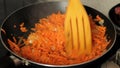 Hashing by a wooden shovel of carrots with onions when frying. Close up. Grated carrots are fried on a frying pan.