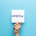 Hashtag MeToo on white paper in hand isolated on blue background. MeToo is a campaign for movement against sexual harassment