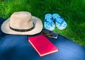 Hat, book sunglasses, flip flops on green grass in the park. Summer holiday concept.