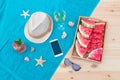 Hat, smartphone, starfishes, seashells, white wine, watermelon, watermelon lemonade and sunglasses on towel on wooden surface.