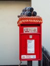 HATHERLEIGH, DEVON, ENGLAND - AUGUST 9 2022: Red post box. It is adorned with crochet tar barrels on sled, part of