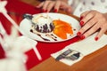 Haute cuisine concept. Woman`s hands with perfect manicure and ice cream brownie sundae with chocolate sauce and slices of date Royalty Free Stock Photo