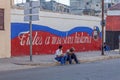 HAVANA, CUBA - APRIL 2, 2012:Cuban teenagers sitting near propaganda graffiti