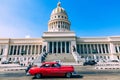 HAVANA, CUBA - DECEMBER 10, 2019: Brightly colored classic American cars serving as taxis pass on the main street in front of the Royalty Free Stock Photo