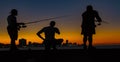 Three men seen in silhouette, fishing from a pier at sundown Royalty Free Stock Photo