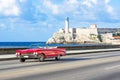 American red 1959 convertible vintage car on the promenade Malecon and in the background the Castillo de los Tres Reyes del Morro