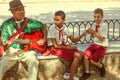 Havana / Cuba - Sept 2018: Old musician plays guitar sitting near to two cuban pupils - boys in red and white uniform Royalty Free Stock Photo