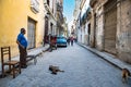 Havana, Street life with dogs, classic car, cycle taxi in small street with view to Capitolio, Cuba