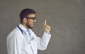 Happy young doctor has an idea and points his finger up on a grey copy space background Royalty Free Stock Photo