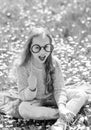 Have a nice day. Girl sits on grass at grassplot, green background. Child posing with cardboard eyeglasses for photo