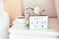 Have a nice day message on lighted box, alarm clock, cup of coffee and flower on the bedside table in sun light. Good morning mood Royalty Free Stock Photo