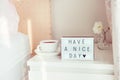 Have a nice day text message on lighted box, cup of coffee and white flower on the bedside table in sun light. Good morning mood. Royalty Free Stock Photo