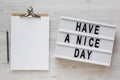 `Have a nice day` words on a modern board, clipboard with blank sheet of paper on a white wooden background, top view. Overhead, Royalty Free Stock Photo