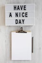 `Have a nice day` words on a modern board, clipboard with blank sheet of paper on a white wooden surface, top view. Overhead, fr Royalty Free Stock Photo