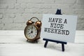 Have a Nice Weekend text and alarm clock on white brick wall and wooden background Royalty Free Stock Photo