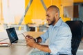 Have a nice working day. Confident young african american businessman working on laptop and talking on cell phone while sitting at Royalty Free Stock Photo