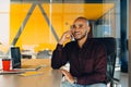 Have a nice working day. Confident young african american businessman working on laptop and talking on cell phone while sitting at Royalty Free Stock Photo