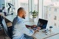 Have a nice working day. Confident young african american businessman working on laptop and talking on cell phone while sitting at Royalty Free Stock Photo