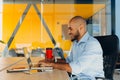 Have a nice working day. Confident young african american businessman working on laptop and talking on cell phone while sitting at Royalty Free Stock Photo