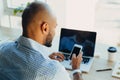 Confident young african american businessman working on laptop and talking on a cell phone while sitting at his workplace in Royalty Free Stock Photo