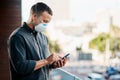 Have no fear, you clients are still here. a young businessman wearing a mask and using a smartphone on the balcony of an