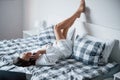 Having conversation. Beautiful girl in white robe lying on the bed at morning time and using smartphone Royalty Free Stock Photo