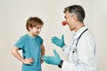 Having fun. Cheerful male pediatrician with clown nose working with happy little boy, standing against grey background