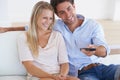 Having fun flipping through the channels. A smiling young couple sitting on a couch and watching television. Royalty Free Stock Photo