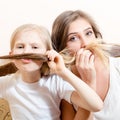 Having fun making mustache beautiful young woman and little blond girl dressed in white shirts sitting on sofa & looking at camera Royalty Free Stock Photo