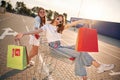 Having fun and riding in a shop cart. Two beautiful women in casual clothes are holding bags, outdoors