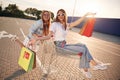 Having fun and riding in a shop cart. Two beautiful women in casual clothes are holding bags, outdoors Royalty Free Stock Photo