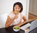 Having a healthy meal thanks to this online recipe. a young woman enjoying a salad and working on a laptop at home. Royalty Free Stock Photo