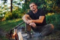 Having a rest. Man in black shirt near the campfire in the forest at his weekend time