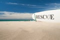 Hawaiian sandy beach with RESCUE sign on surfboard on sand with sea and blue sky beyond.1