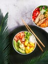 Hawaiian trendy poke bowls salmon, heura soy protein or vegan chicken, variety vegetables, served in bowl on tropical leaves.