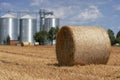 Round Hay Bales on the Field After Harvest Against Grain Silos Royalty Free Stock Photo