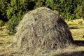 Hay stack on a field nearby a plum trees orchard - Image . Close-up of a single big haystack near green forest in summer season Royalty Free Stock Photo