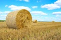 Hay wrapped in a bale lies in a field under a blue sky with clouds Royalty Free Stock Photo