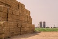 Haystack in front of two cylindrical silos on a farm. Stack of Rectangular Bales of dry straw in the open air. Agribusiness