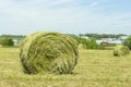 A haystack of straw twisted into a roll on a field. The village is visible on the horizon. Hay harvest