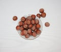 Hazelnuts in the shell, lying in a small white plate on a light background.