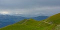 Hazy mountains with green meadow and dark peaks in the distance under a dark cloudy sky in the Alps Royalty Free Stock Photo