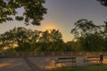 HDR image of a sun setting down in the evening behind the trees in a park with comfortable old benches in the foreground Royalty Free Stock Photo