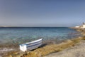 HDR photo of a sunny day at the sea coast with deep blue clean water and a nice stone beach and a small white boat in front Royalty Free Stock Photo