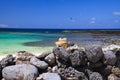 Head of blonde woman with straw hat sitting behind wall of piled natural rocks on beach with turquoise ocean Royalty Free Stock Photo